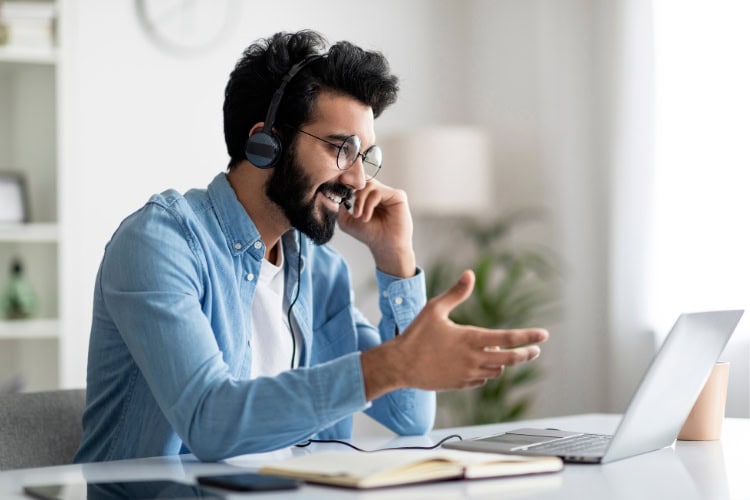 Man sitting at a desk looking at a laptop while wearing a telephone headset.